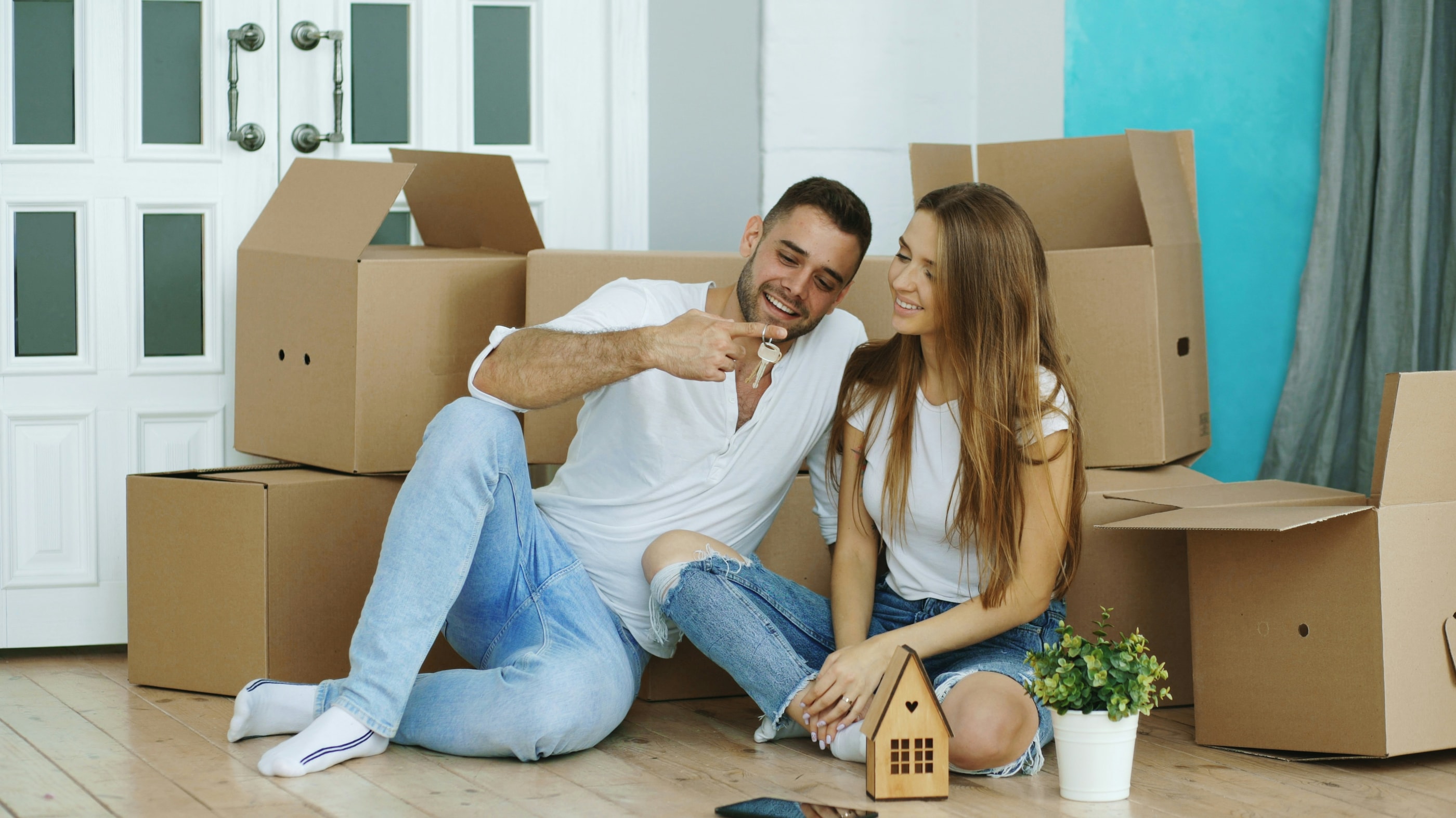 Casal sentado entre caixas de mudança, ele mostrando a chave do apartamento novo